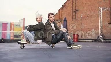 朋友们在户外坐在滑板上玩得很开心。 年轻的时髦情侣玩得很开心
